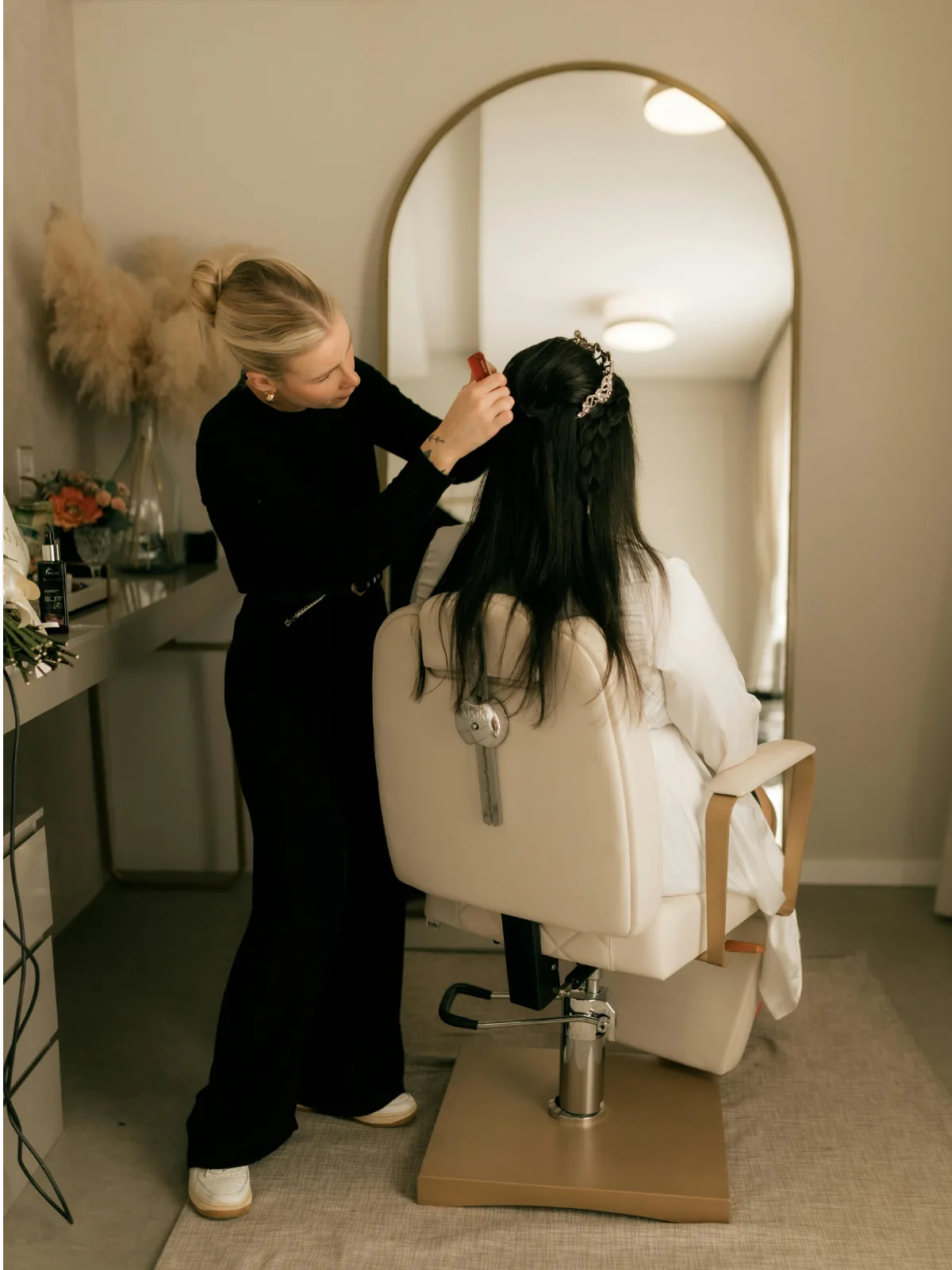 A stylist pinning a section at the chair, arched mirror behind